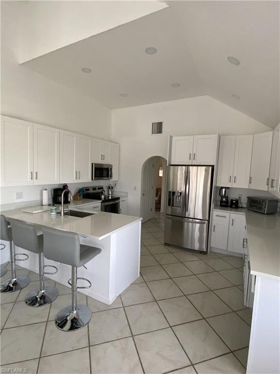 Kitchen featuring white cabinets, a breakfast bar, stainless steel appliances, a peninsula, and arched walkways