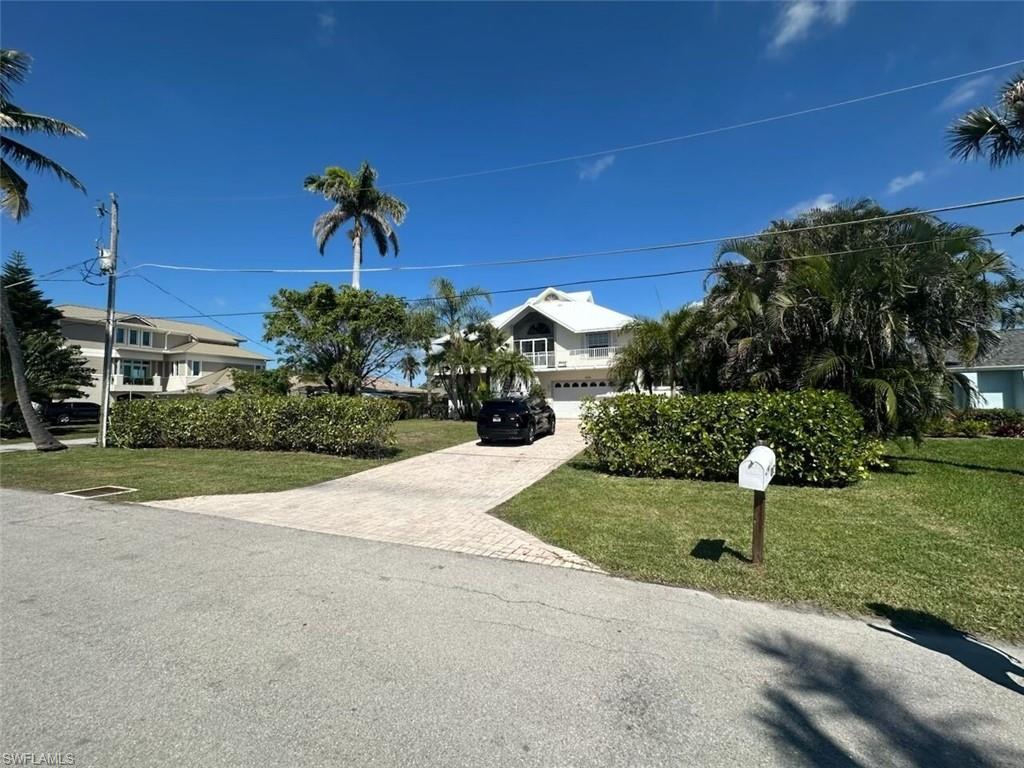 View of property hidden behind natural elements featuring a front lawn, decorative driveway, a garage, and a residential view