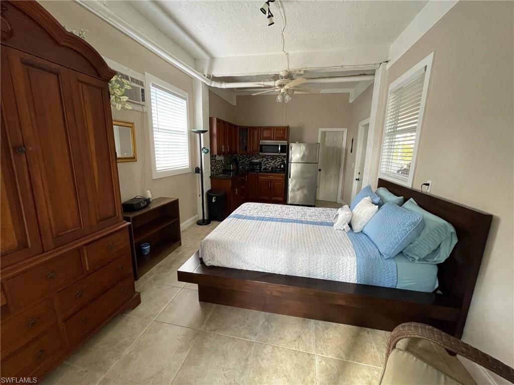 Bedroom with a textured ceiling, freestanding refrigerator, multiple windows, light tile patterned flooring, and a ceiling fan