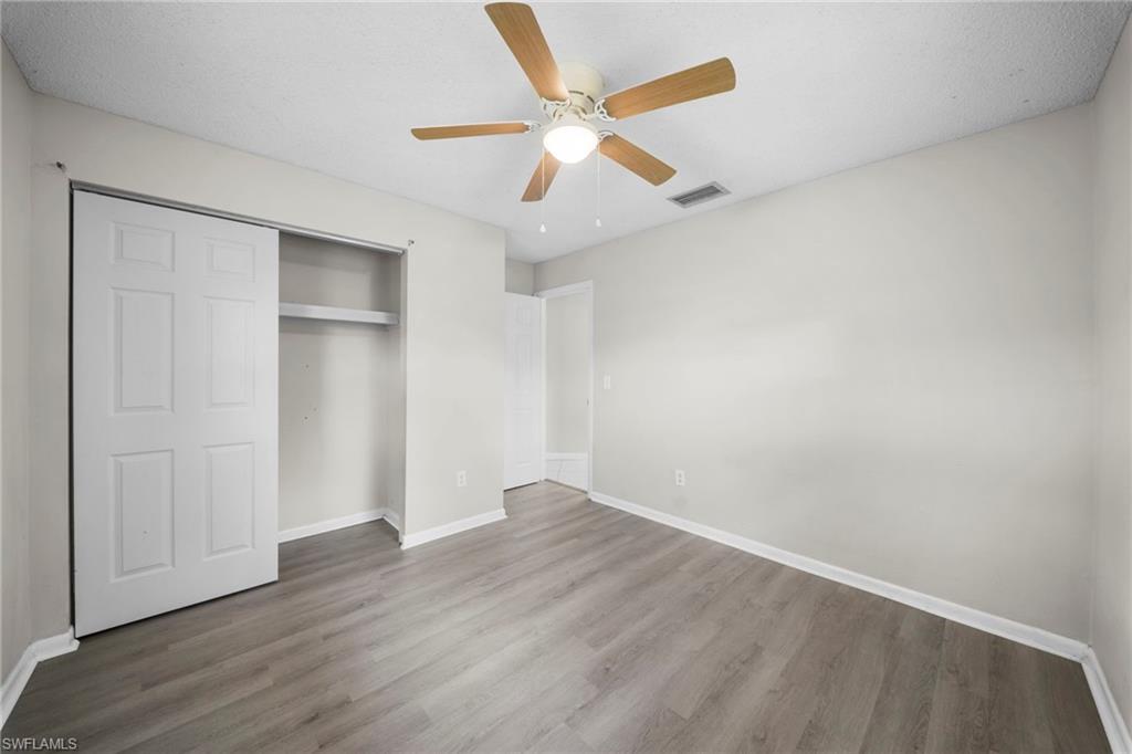 Wood-finish flooring, white walls, ceiling fan with light, and sliding closet doors