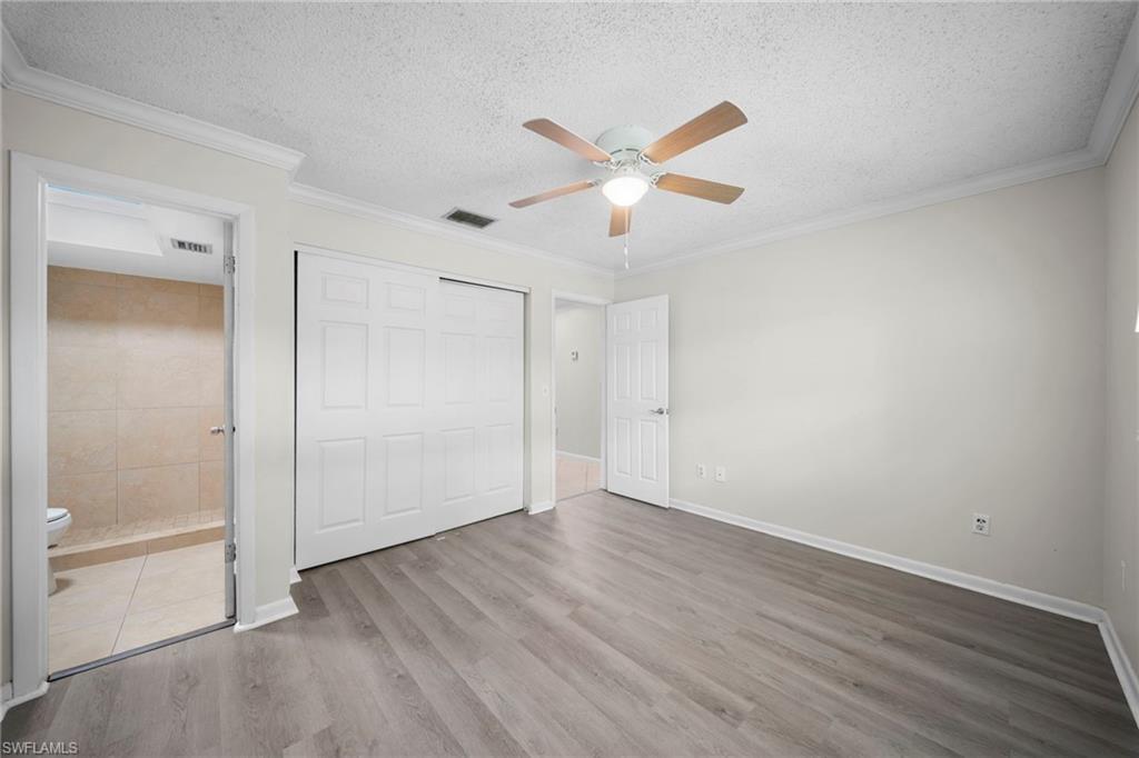 Crown molding, wood-finish flooring, ceiling fan with light fixture, sliding panel closet doors, and a tiled shower with toilet