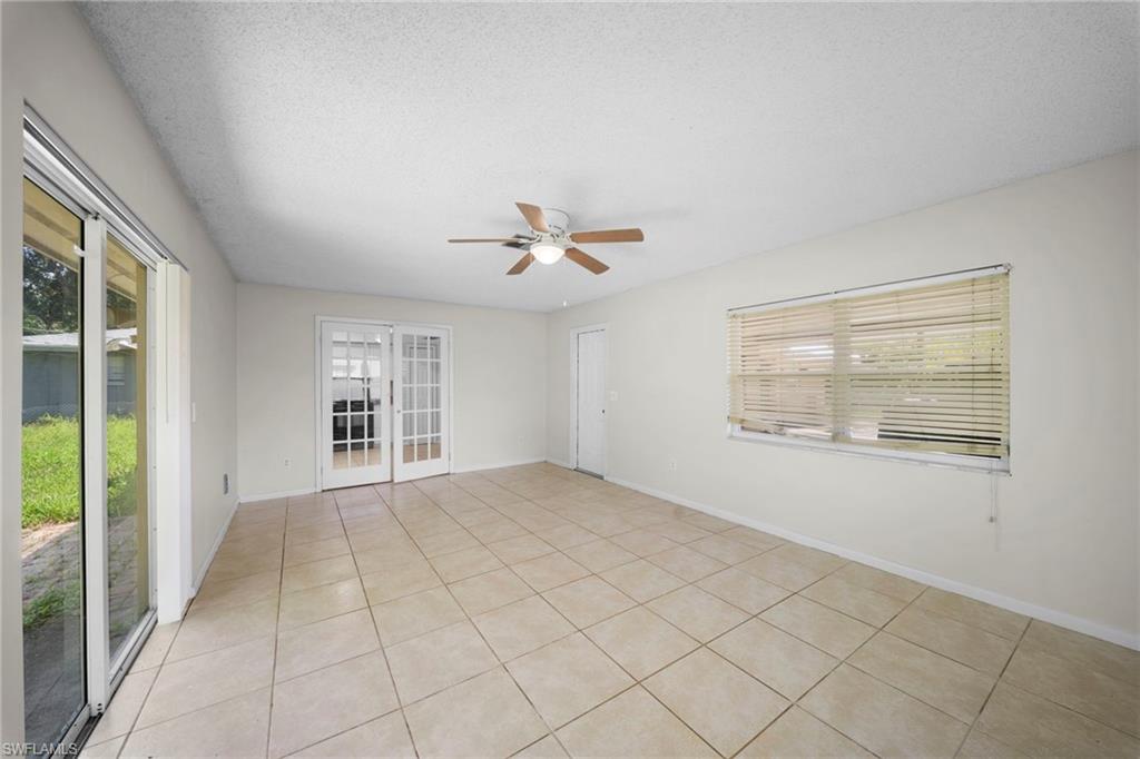Neutral-toned tile flooring, French doors with glass panels, large window with horizontal blinds, sliding glass door, and a ceiling fan with light fixture
