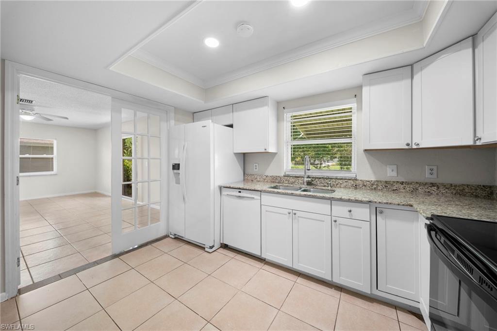 White shaker cabinetry, light-toned tile flooring, recessed lighting, and a white French door