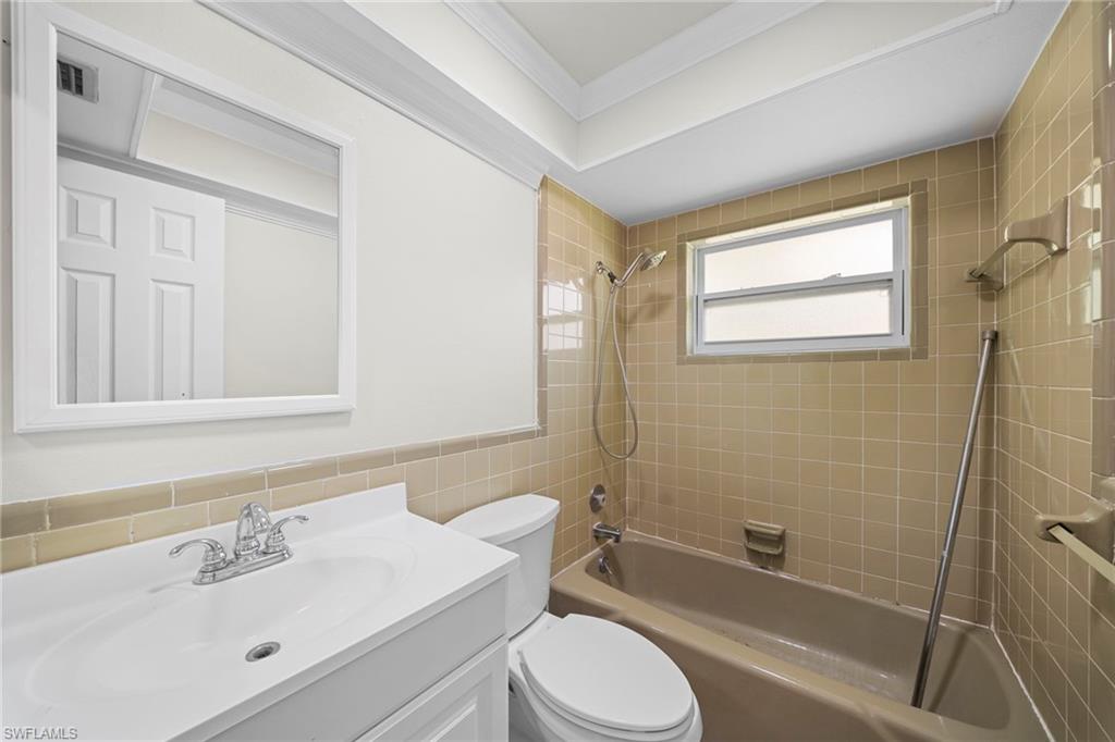 Vanity with integrated sink and chrome faucet, rectangular wall-mounted mirror, ceramic tile bath surround, and window with privacy glazing