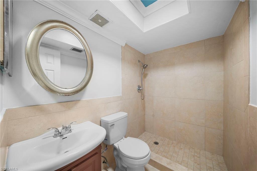 Walk-in shower with tiled walls and floor, vanity with integrated sink, and an overhead skylight