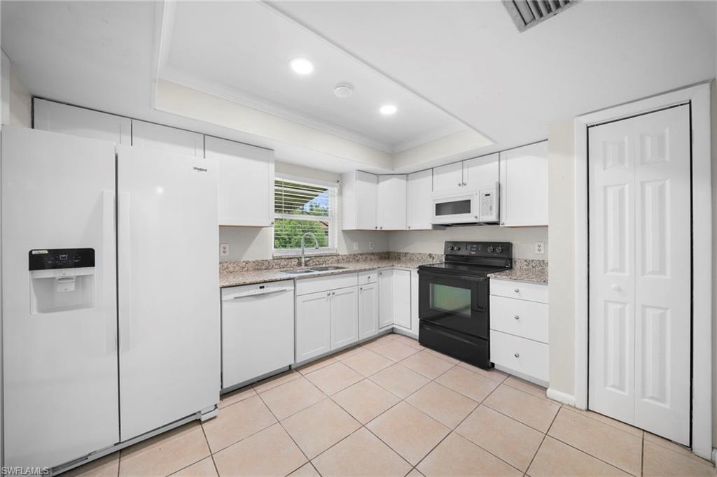 Kitchen featuring white cabinetry, light-toned tiled flooring, white appliances, and light speckled countertops