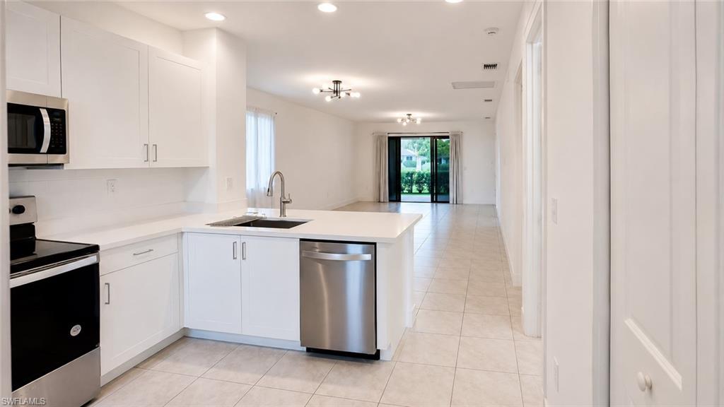 Well-appointed kitchen featuring white cabinetry, stainless steel appliances, a large basin sink, and ample countertop space