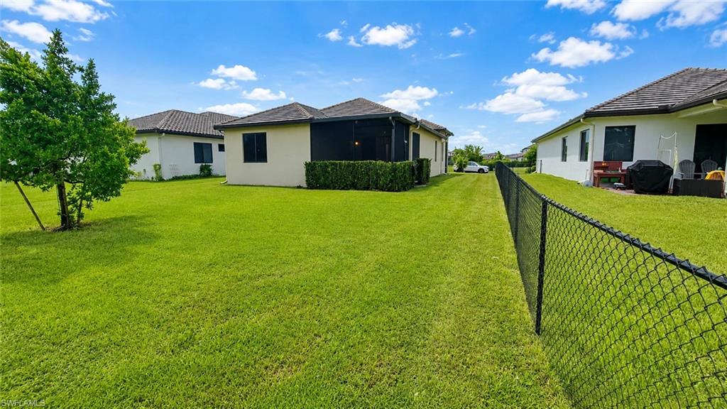 Expansive lawn space featuring a black chain-link fence, mature shrubbery, and a screened lanai with a tiled roof