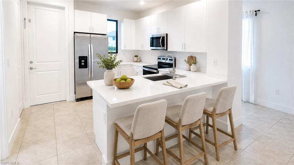 Modern kitchen featuring white cabinetry, stainless steel appliances, a center island with countertop seating, and tile flooring