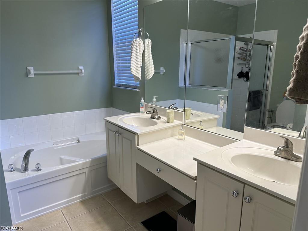 Dual vanity with integrated sinks, built-in vanity seating, full-width mirror, and a corner soaking tub with tile surround