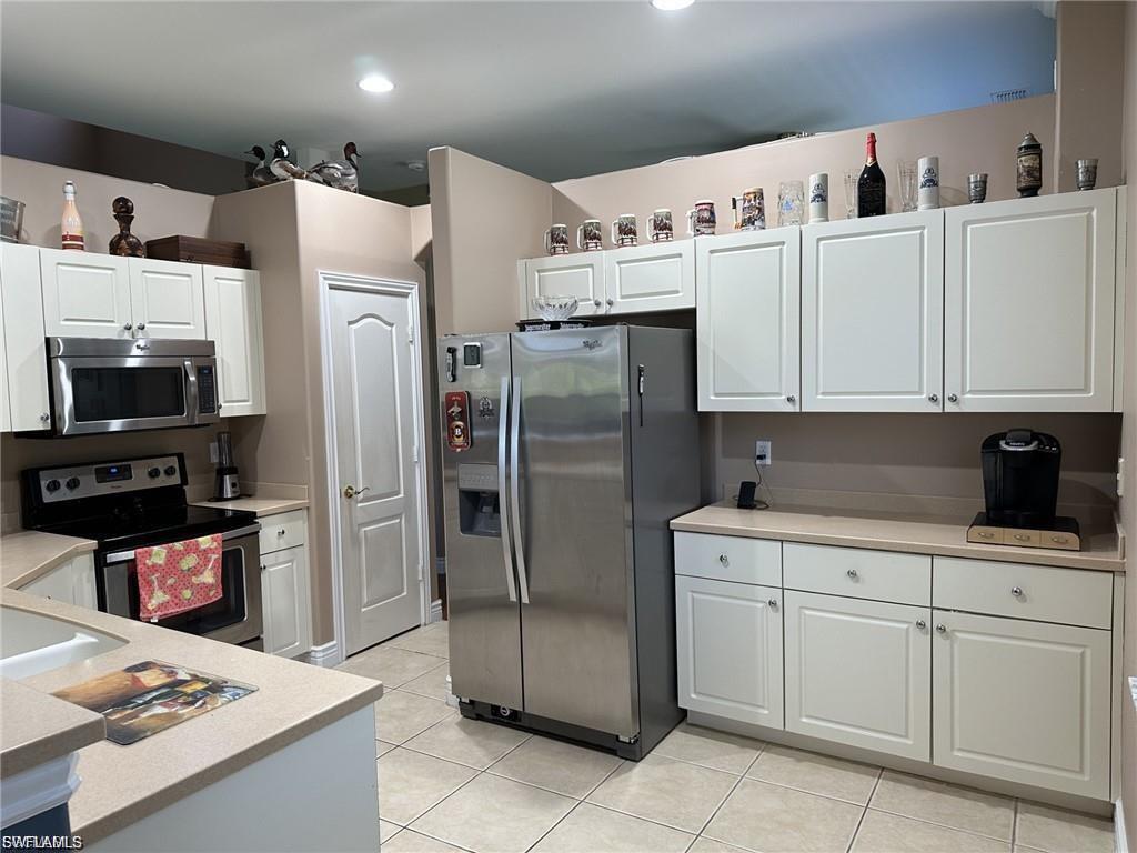 White paneled cabinetry, stainless steel appliances, neutral countertops, tile flooring, and recessed lighting