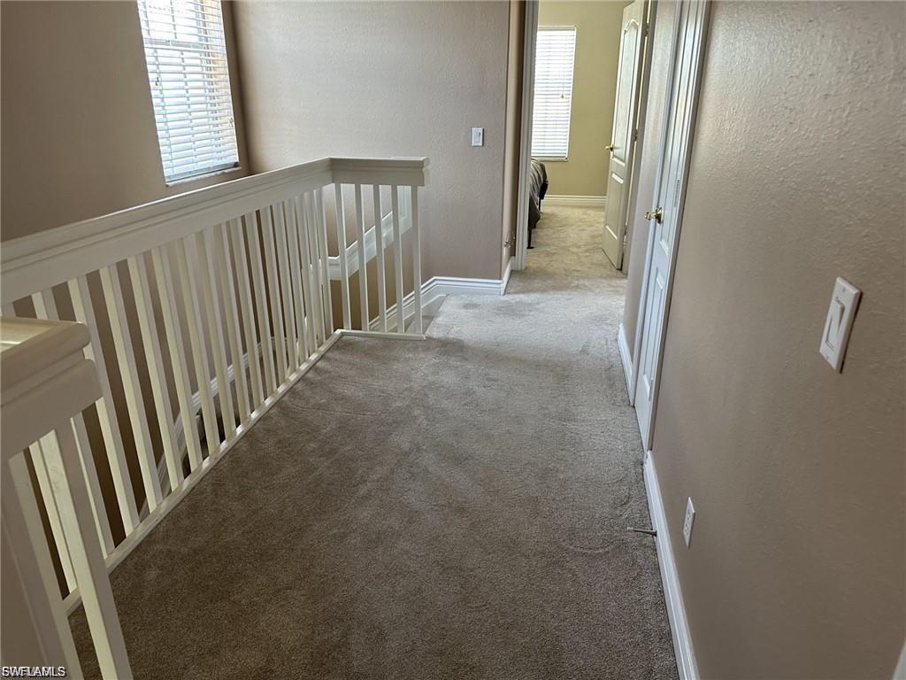 Light beige wall paint, white painted banister, neutral tone carpeting, white baseboards, and white interior doors