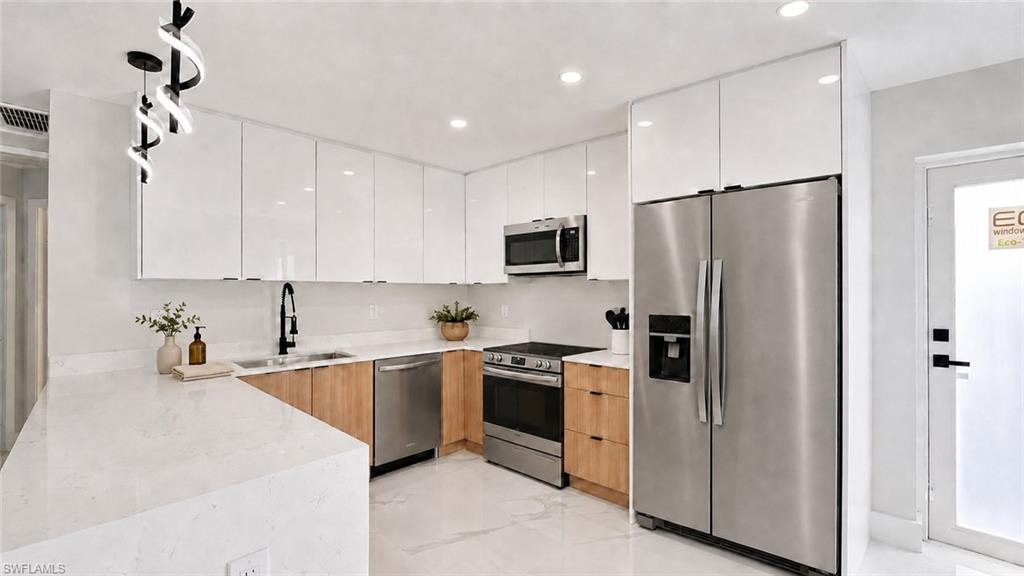 Modern kitchen featuring white gloss cabinetry, light wood-finish lower cabinets, stainless steel appliances, white countertops, and a contemporary pendant light fixture