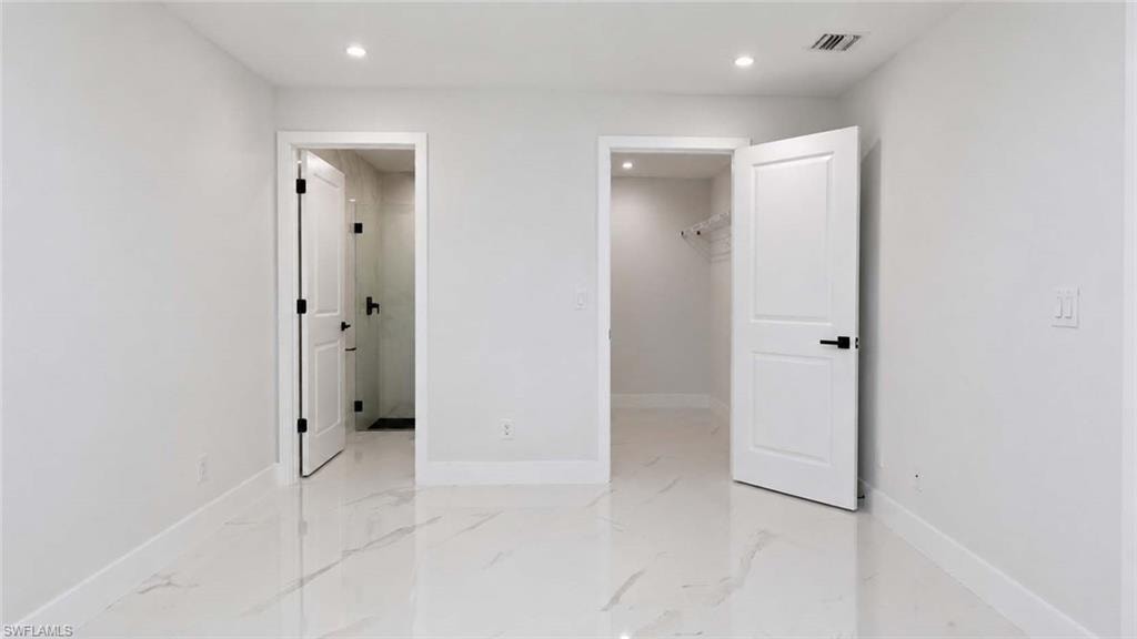 White walls with recessed lighting, marble-finish tile flooring, white trim, and white two-panel doors with black hardware