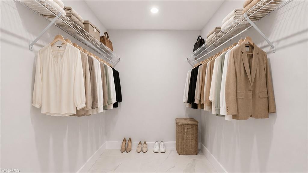 Dedicated walk-in closet featuring dual wall-mounted clothing rods with coordinating wooden hangers, white shelving system, white finish flooring, recessed ceiling lighting, and woven storage basket for organized garment and accessory storage
