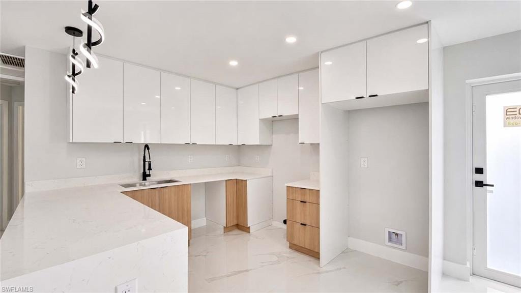 Modern kitchen featuring white glossy upper cabinetry, wood-finish lower cabinetry, white stone countertops, and a contemporary pendant light fixture