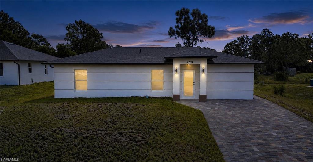 Modern exterior with a light-colored facade, dark trim, and a multi-toned paver driveway