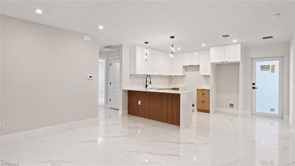 Open-concept space featuring large format tile flooring, recessed lighting, white upper cabinetry, a kitchen island with a slatted wood-finish panel, and pendant lighting