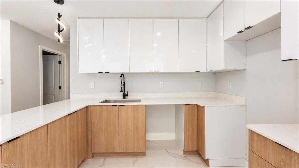 U-shaped kitchen with white stone countertops, wood-finish lower cabinetry, white upper cabinetry, and a matte black faucet