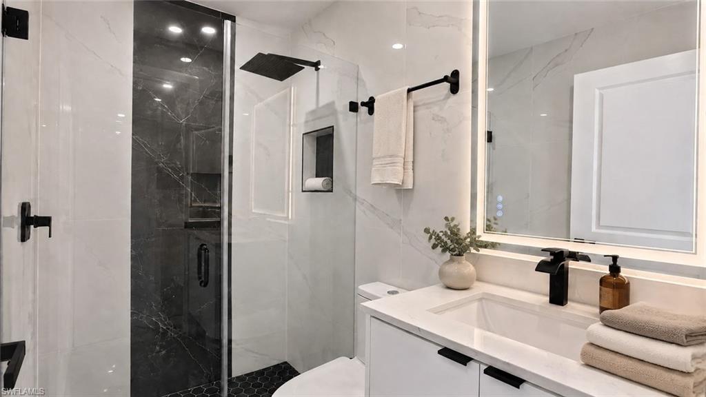Contemporary bathroom featuring a glass-enclosed shower, black hexagonal floor tile, and a floating vanity with a single basin sink