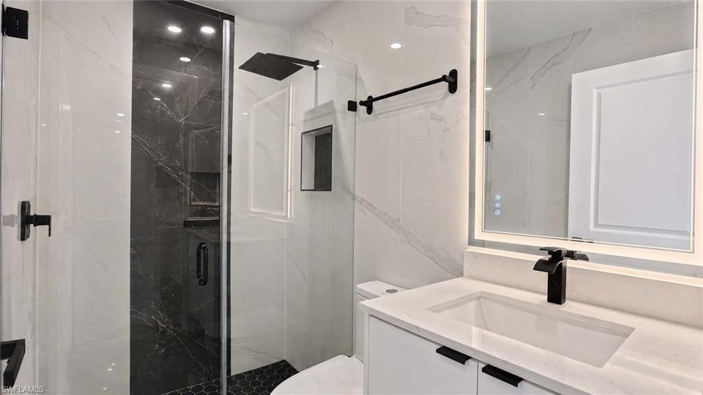Glass-enclosed shower with dark tile accent, rainfall shower head, and matte black fixtures