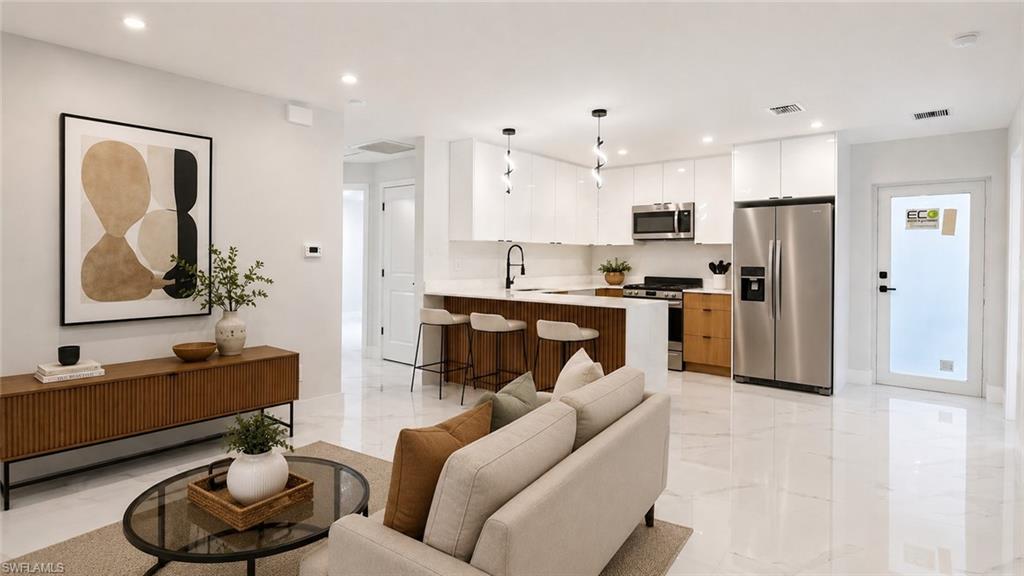 Open-concept living space featuring high-gloss white cabinetry, stainless steel appliances, a wood-finish island with seating, and bright tile flooring