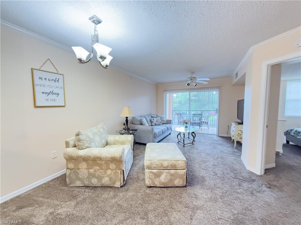 Living room with crown molding, carpet flooring, a chandelier, a textured ceiling, and ceiling fan