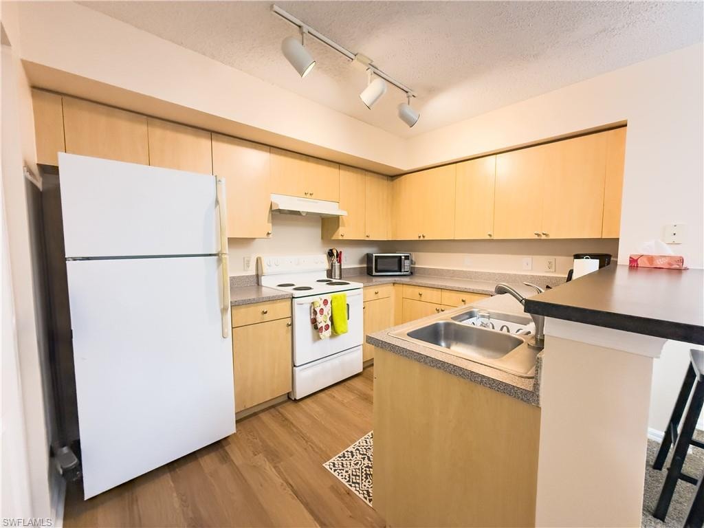 Kitchen featuring white appliances, a peninsula, track lighting, light brown cabinetry, and a textured ceiling