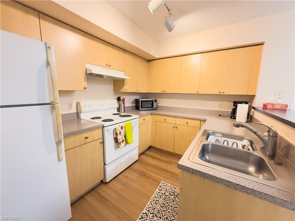 Kitchen with white appliances, light brown cabinetry, light wood finished floors, under cabinet range hood, and track lighting