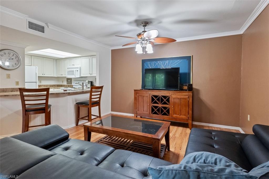 Hardwood flooring, crown molding, ceiling fan, white upper and lower cabinetry, and a kitchen pass-through with stone-finish countertop