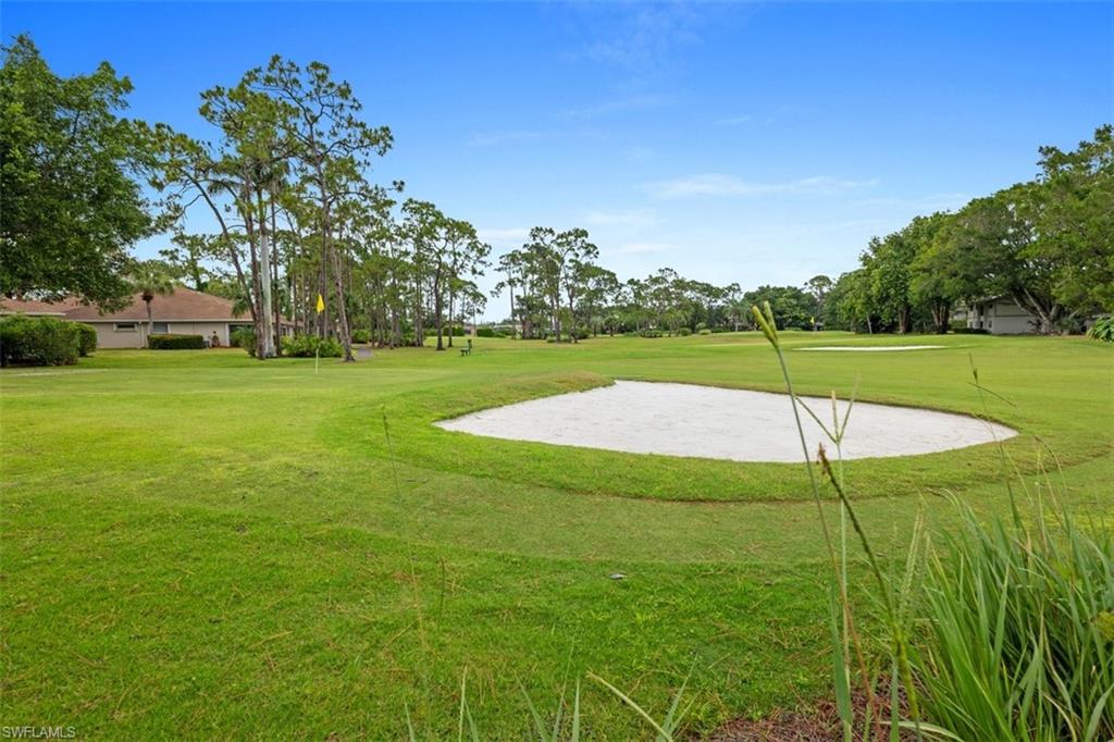 Lush green expanse featuring a sand trap, putting green with flag, and mature trees bordering the area