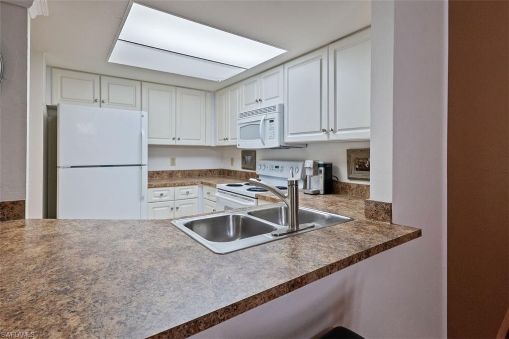 Kitchen featuring white cabinetry, a dual basin stainless steel sink, a counter-mounted faucet, and a pass-through counter