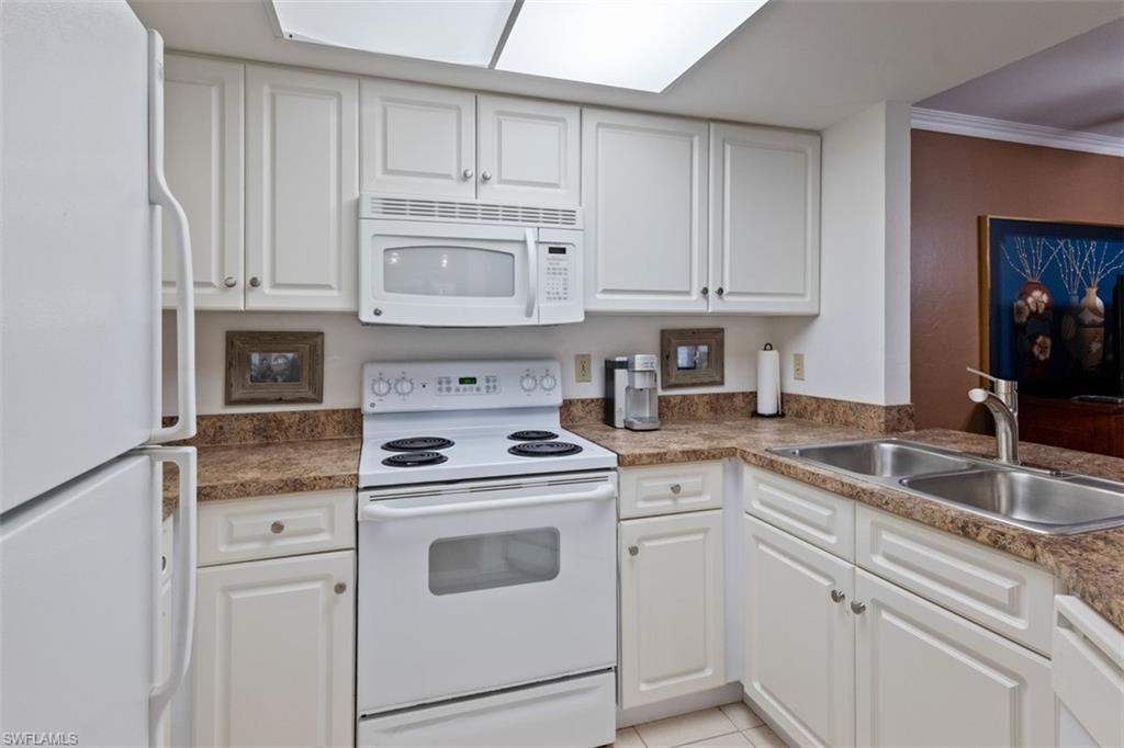 Kitchen featuring white cabinetry, white appliances, a dual basin stainless steel sink, and light-colored countertops