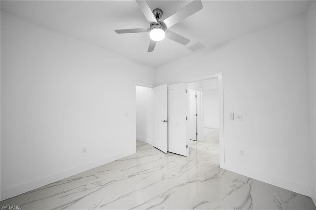 White walls with a ceiling fan, dual doors, and marble-look flooring