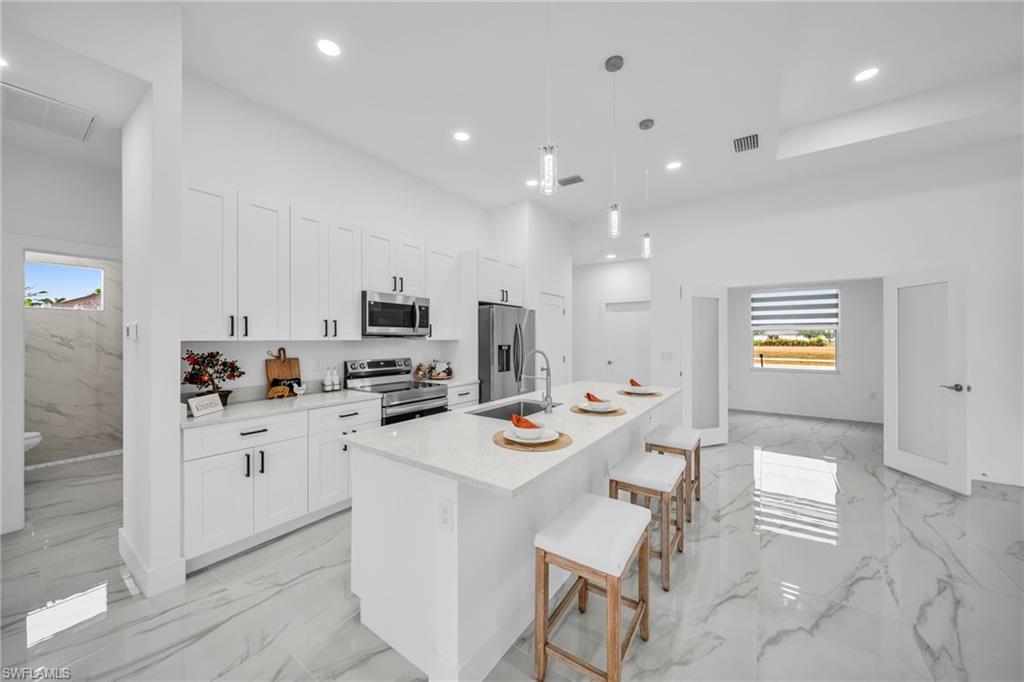 Modern kitchen featuring white shaker cabinetry, stainless steel appliances, a center island with pendant lighting, and polished tile flooring