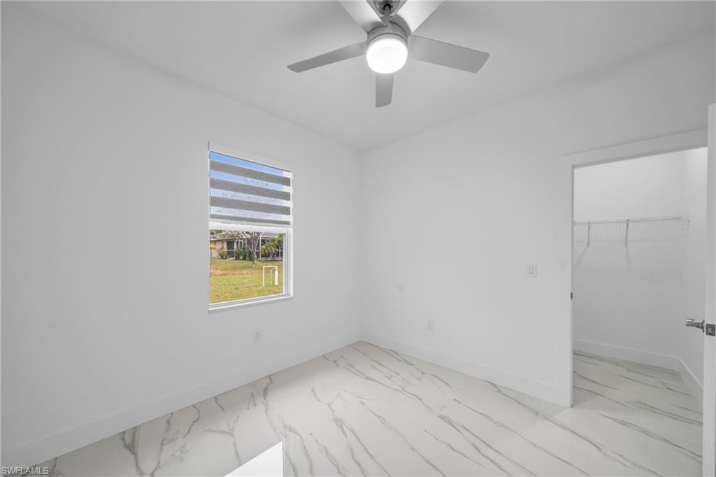 White walls, marble-finish tile flooring, ceiling fan with integrated lighting, window with horizontal blinds, and a closet with wire shelving