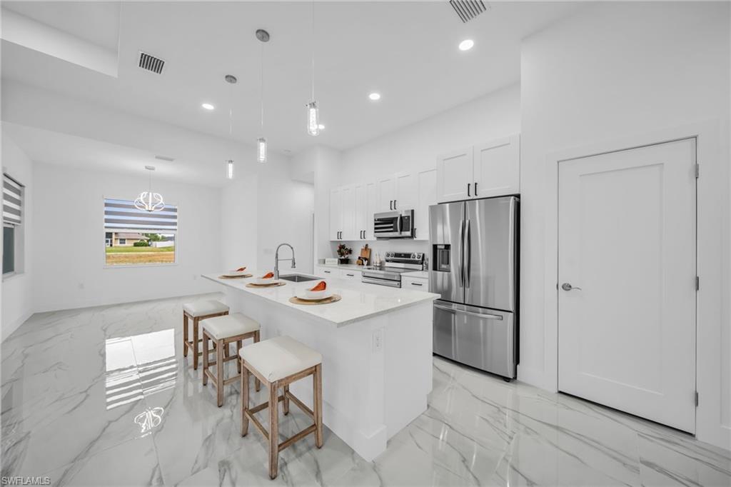 Kitchen with white cabinetry, stainless steel appliances, a center island with a sink, and pendant lighting