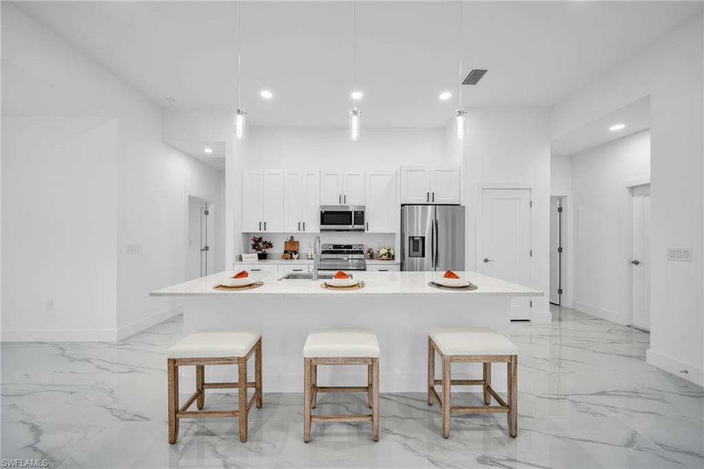 Kitchen featuring an expansive island with countertop seating, stainless steel appliances, white cabinetry, and pendant lighting over the island