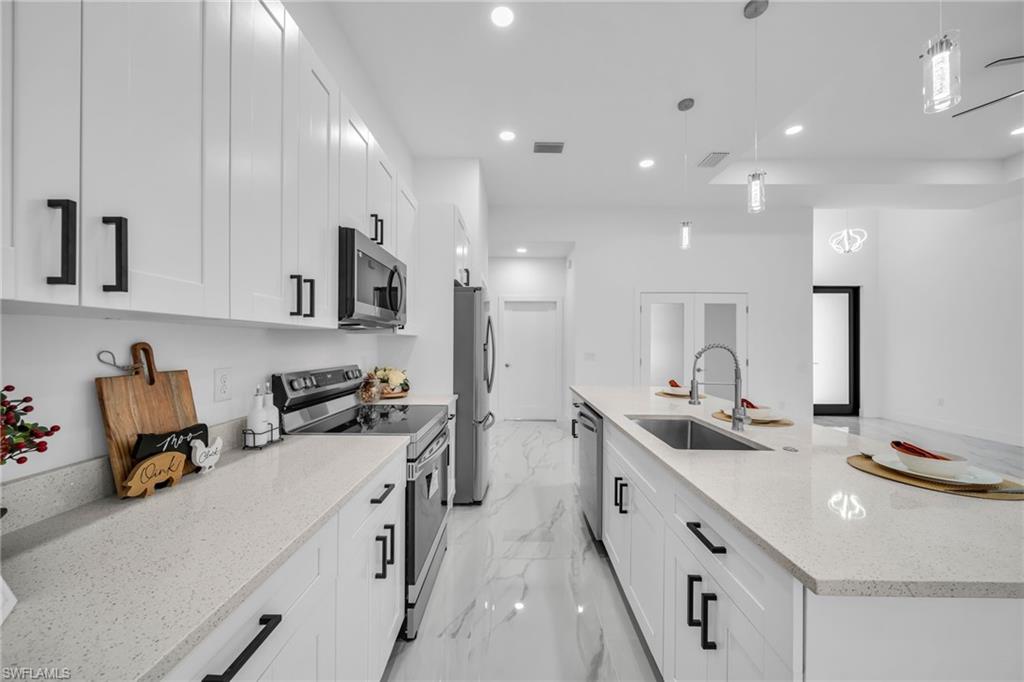 Bright kitchen featuring white shaker cabinetry, stainless steel appliances, a large center island with an undermount sink, and recessed lighting