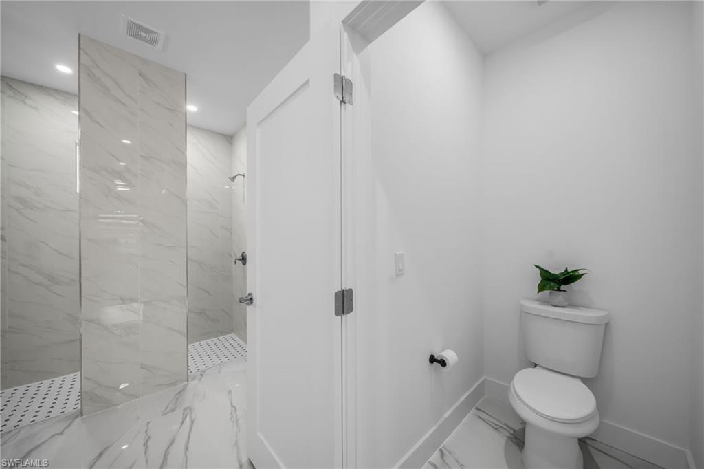 White wall paneling, full-height tile shower, glass shower partition, white toilet, and recessed lighting