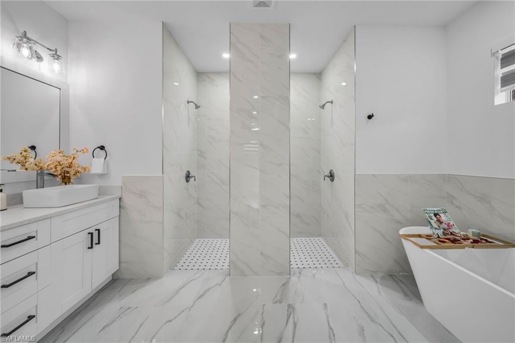 Dual walk-in showers with glass partitions, a freestanding soaking tub, single vanity with a vessel sink, and large format tile flooring