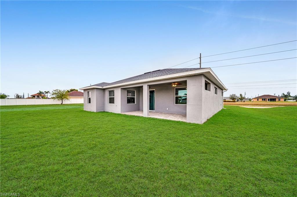 Expansive grassy lawn with a covered patio featuring a ceiling fan and exterior lighting