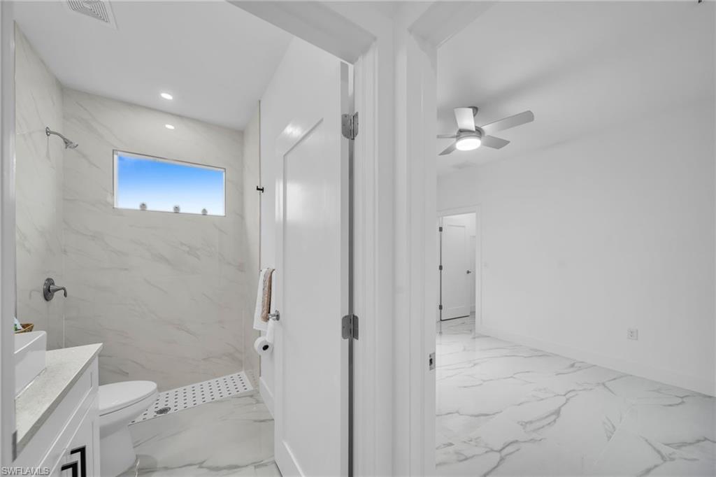 Recessed lighting, tile shower surround, ceiling fan, white wall paint, and white tile flooring