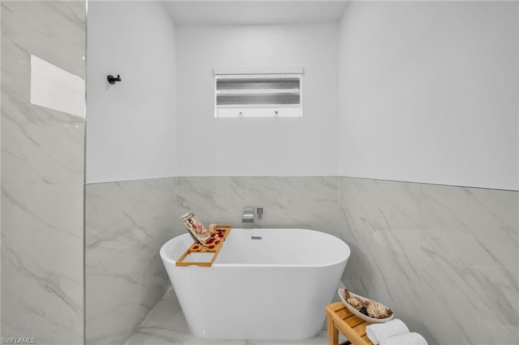 Freestanding soaking tub with a wall-mounted faucet, complemented by large format tile walls and a privacy window with blinds