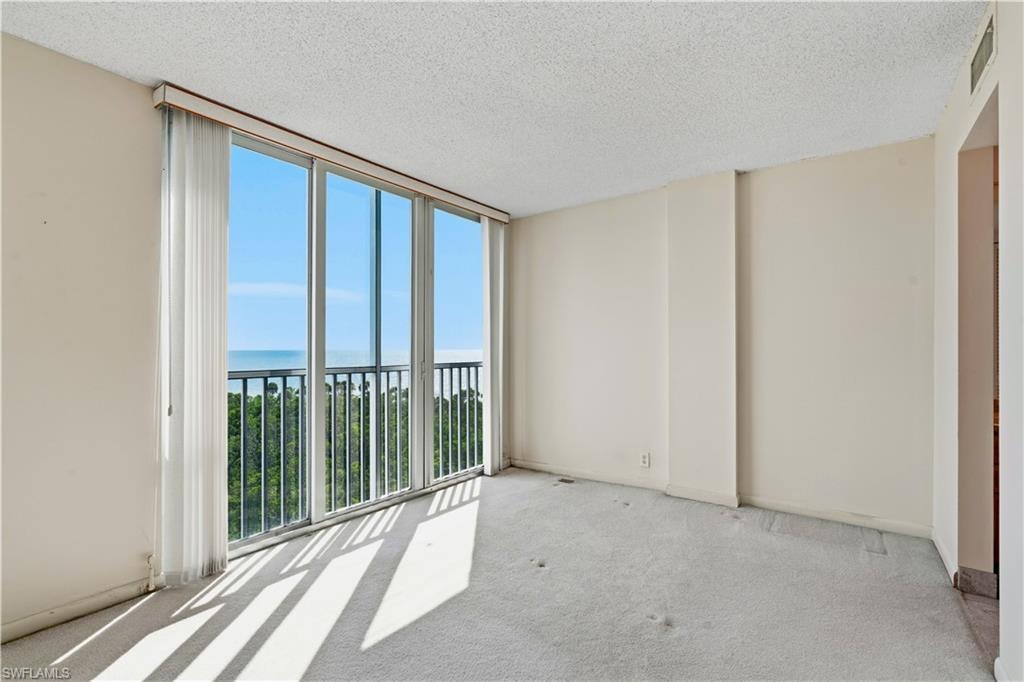 Expansive wall of windows with a balcony, offering a high-level ocean and tree canopy backdrop