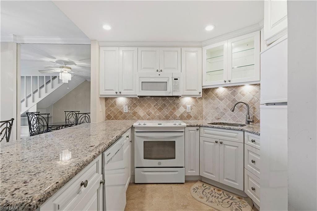 White cabinetry with under-cabinet lighting, granite countertops, tile backsplash, and built-in appliances