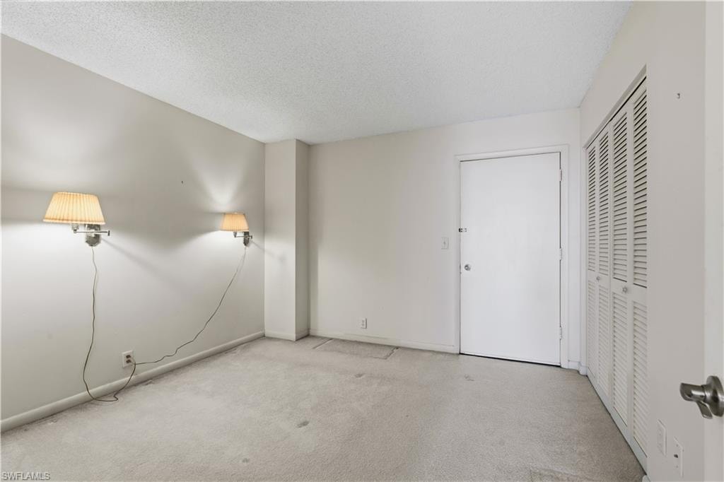 Textured ceiling, wall-mounted sconces, neutral wall paint, white entry door, and bi-fold louvered closet doors