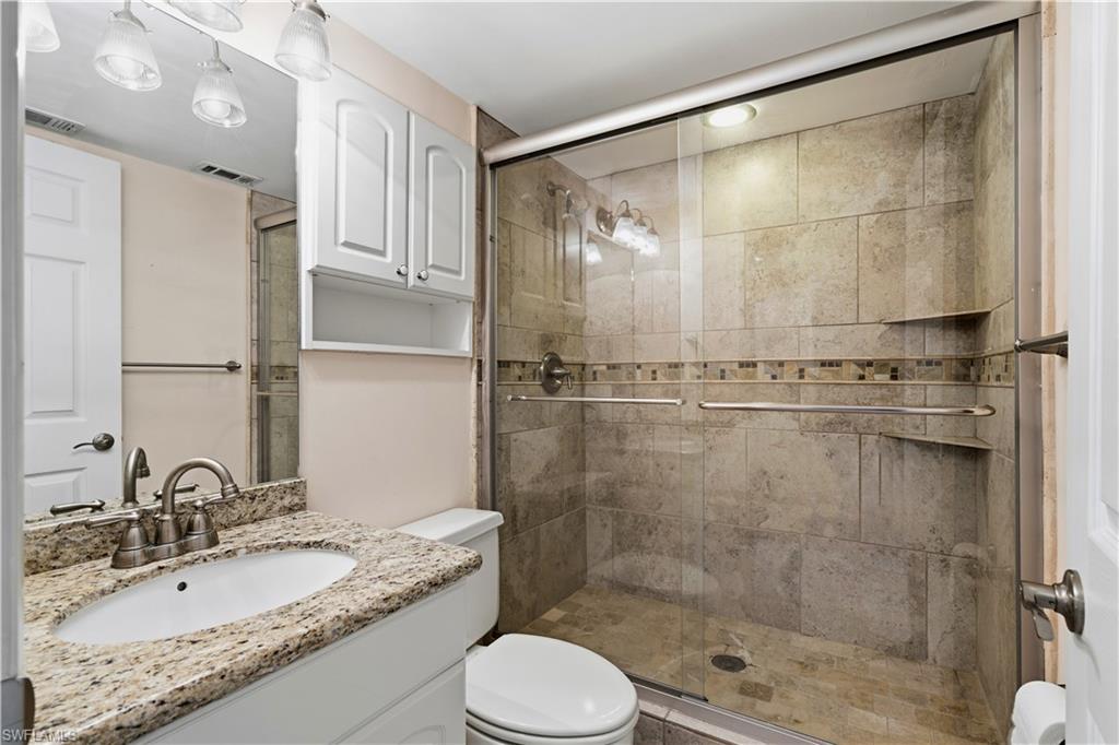 Bathroom vanity with a speckled countertop, a large mirror, white cabinetry, and a walk-in shower with tiled walls
