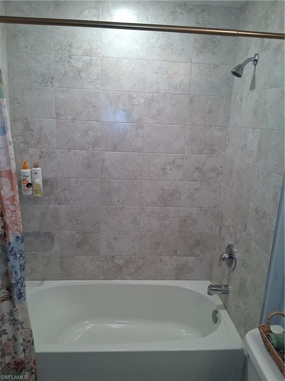 White bathtub with chrome fixtures and light-toned tiled shower surround