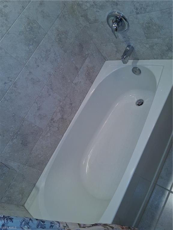 White bathtub with chrome fixtures and grey rectangular tile surround
